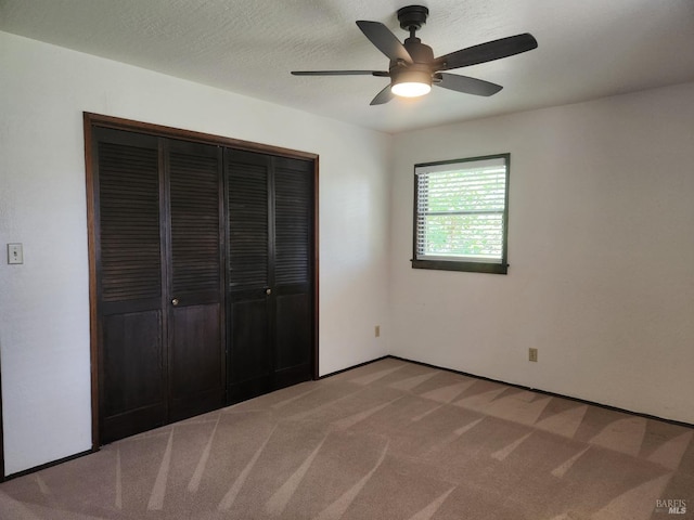 unfurnished bedroom featuring a closet, a textured ceiling, baseboards, ceiling fan, and light colored carpet