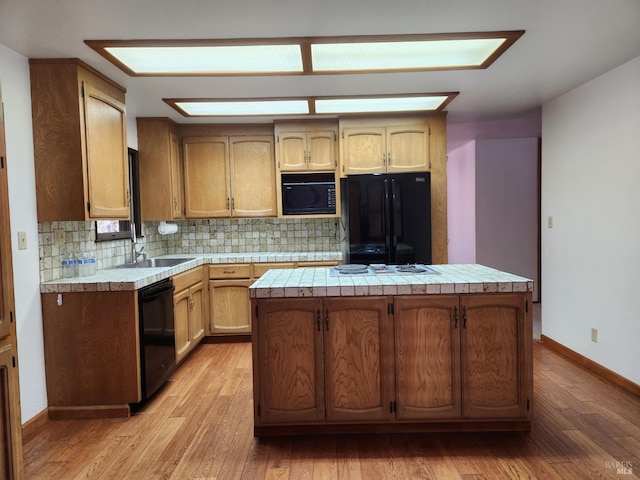 kitchen featuring decorative backsplash, a center island, light wood-type flooring, black appliances, and a sink