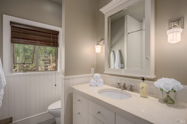 bathroom featuring wainscoting, toilet, walk in shower, and vanity