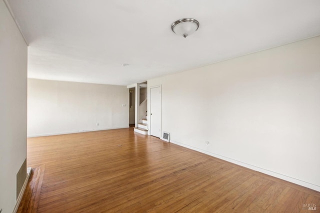 empty room with stairs, wood finished floors, visible vents, and baseboards