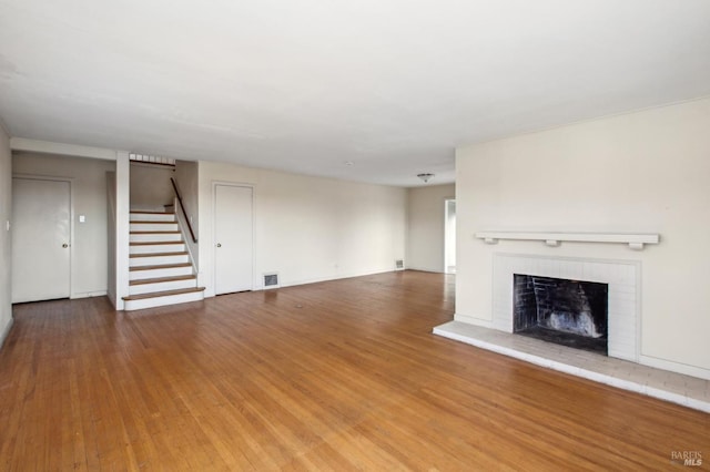 unfurnished living room featuring visible vents, a fireplace, stairs, and wood finished floors