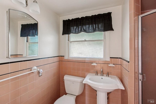 bathroom with a wainscoted wall, a sink, a shower stall, tile walls, and toilet