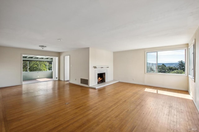 unfurnished living room featuring a wealth of natural light, light wood-style floors, a lit fireplace, and visible vents