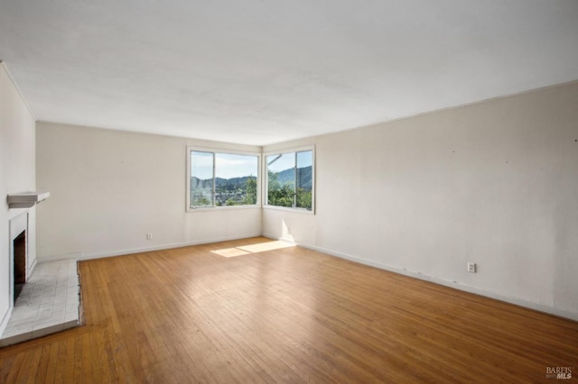 unfurnished living room with a fireplace with raised hearth, baseboards, and wood finished floors