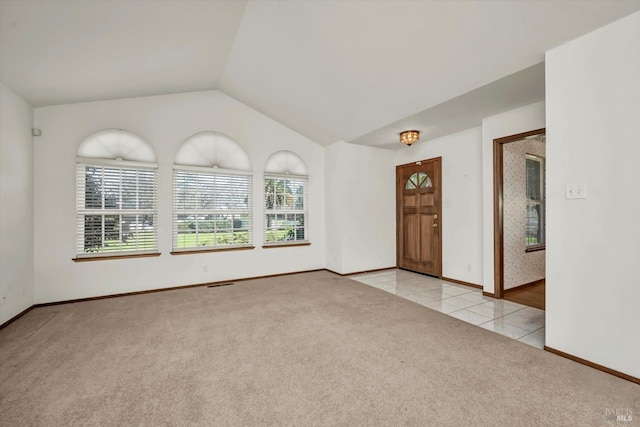 spare room featuring light colored carpet, visible vents, light tile patterned flooring, vaulted ceiling, and baseboards