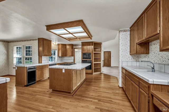 kitchen with tile countertops, a sink, light wood-style floors, black appliances, and wallpapered walls