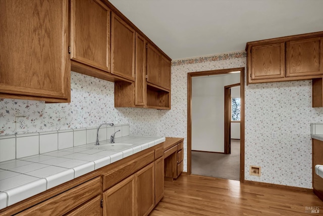 kitchen featuring light wood-type flooring, brown cabinets, a sink, and wallpapered walls