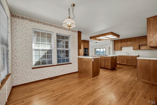 kitchen featuring light wood-style flooring, a peninsula, black appliances, brown cabinetry, and wallpapered walls