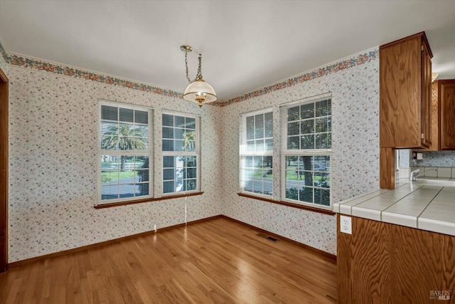 unfurnished dining area featuring baseboards, wood finished floors, visible vents, and wallpapered walls