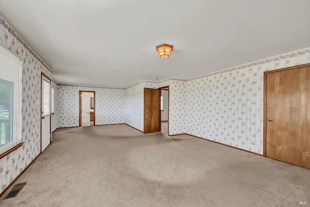 carpeted spare room featuring baseboards, visible vents, and wallpapered walls