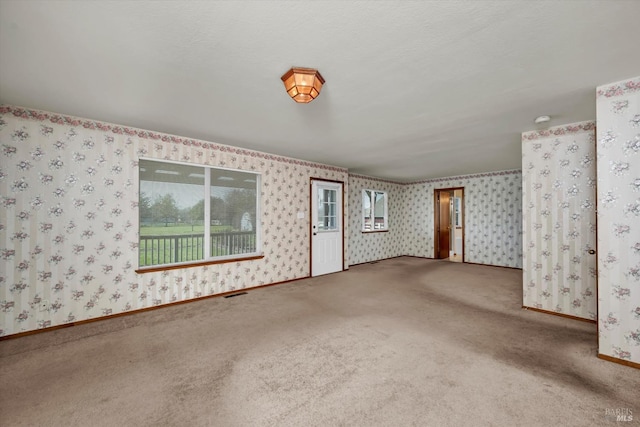 spare room with carpet floors, visible vents, a textured ceiling, baseboards, and wallpapered walls