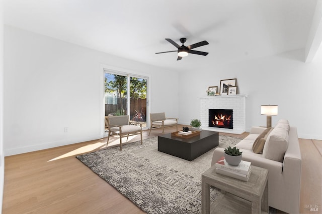 living area with a brick fireplace, wood finished floors, a ceiling fan, and baseboards