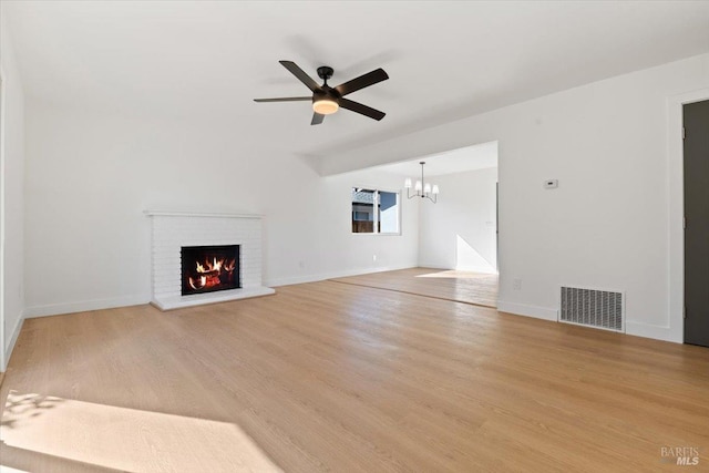 unfurnished living room with ceiling fan with notable chandelier, a fireplace, visible vents, baseboards, and light wood-type flooring