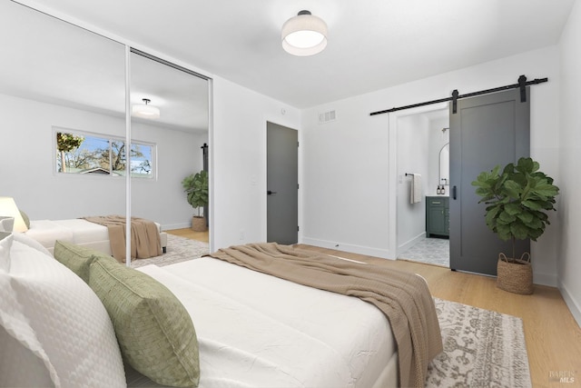 bedroom featuring a barn door, visible vents, baseboards, light wood-style floors, and a closet