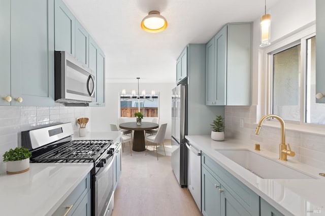 kitchen featuring pendant lighting, stainless steel appliances, light countertops, a sink, and blue cabinets