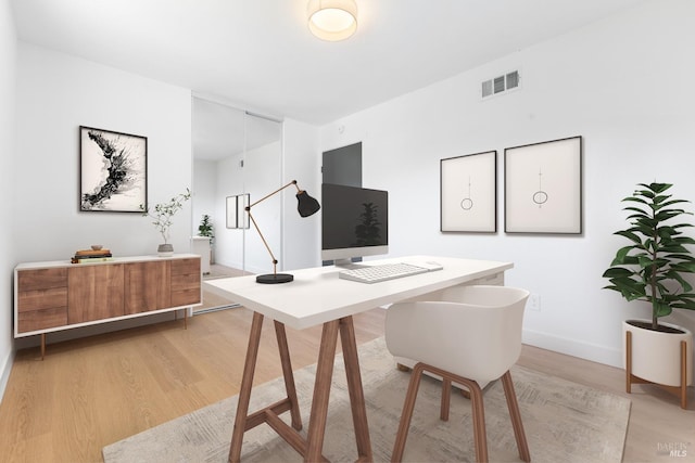 office space with light wood-type flooring, visible vents, and baseboards