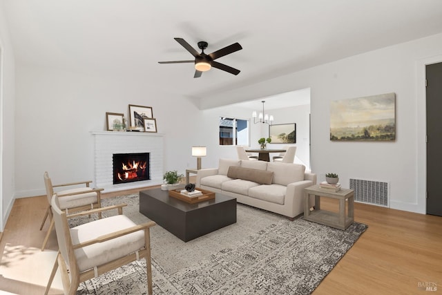 living area with ceiling fan with notable chandelier, a fireplace, wood finished floors, and visible vents