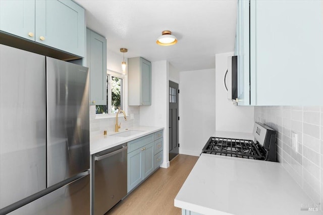 kitchen with appliances with stainless steel finishes, light countertops, light wood-type flooring, blue cabinetry, and a sink