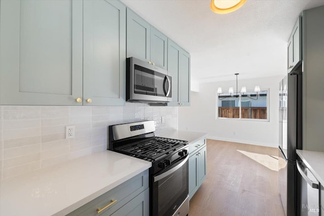 kitchen featuring light countertops, backsplash, appliances with stainless steel finishes, light wood-style floors, and a chandelier