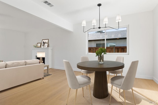 dining room featuring baseboards, a brick fireplace, visible vents, and light wood-style floors