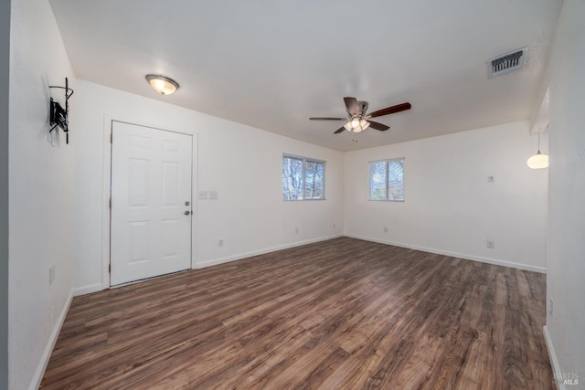 empty room with dark wood-style floors, visible vents, baseboards, and a ceiling fan