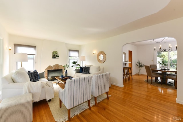 living room with arched walkways, a notable chandelier, a fireplace, baseboards, and light wood-style floors