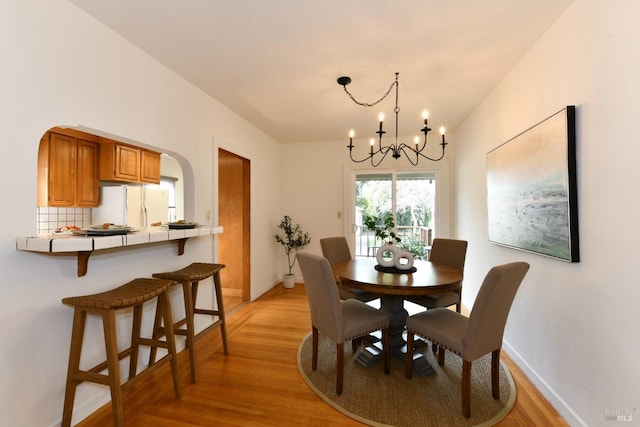 dining area featuring arched walkways, light wood-type flooring, a notable chandelier, and baseboards