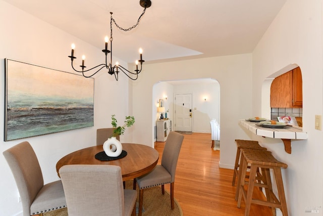 dining room with light wood-type flooring, baseboards, arched walkways, and a notable chandelier