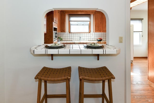 kitchen with tile countertops, a kitchen bar, backsplash, and light wood-style floors