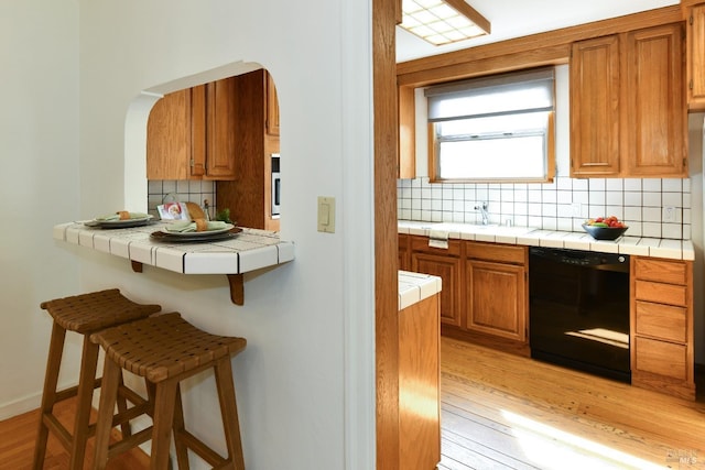 kitchen featuring tile counters, tasteful backsplash, light wood-type flooring, dishwasher, and a kitchen breakfast bar