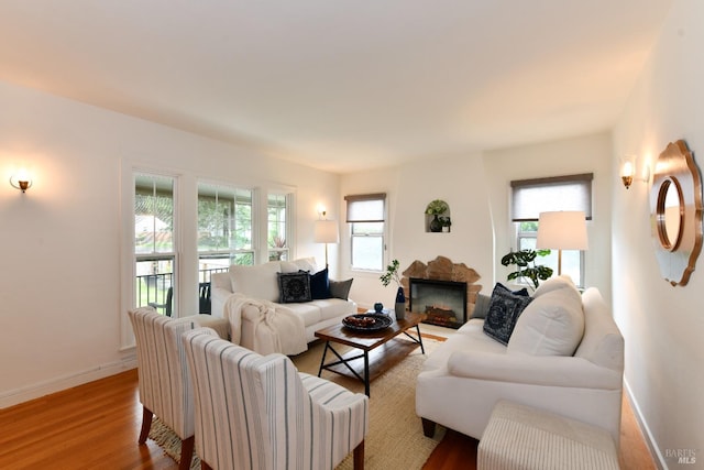 living area with a wealth of natural light, a fireplace, baseboards, and wood finished floors