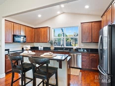 kitchen featuring stainless steel appliances, dark wood-style flooring, a sink, vaulted ceiling, and dark countertops