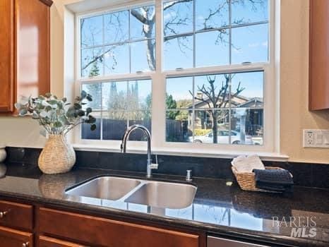 kitchen featuring a healthy amount of sunlight, brown cabinets, a sink, and dark stone countertops