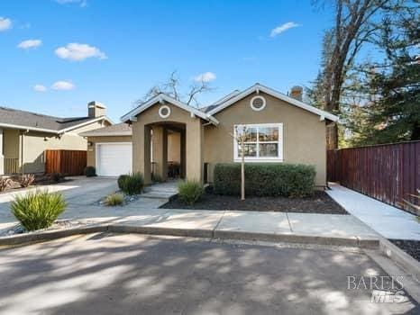 view of front of home with stucco siding, driveway, an attached garage, and fence