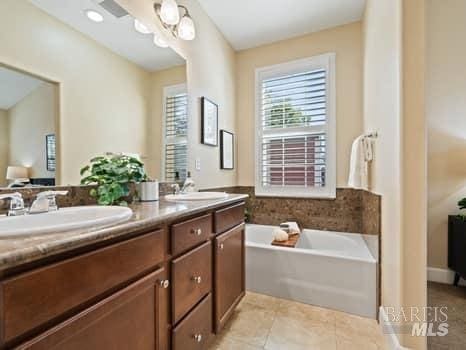 ensuite bathroom featuring double vanity, connected bathroom, a sink, tile patterned flooring, and a bath