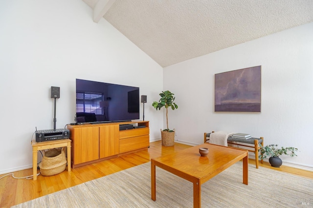 living area with vaulted ceiling with beams, a textured ceiling, and light wood-type flooring