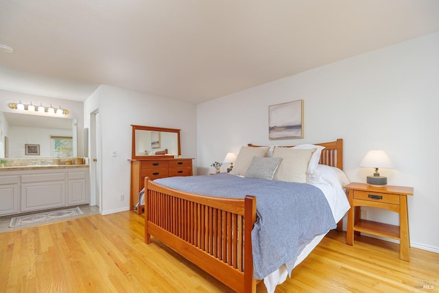 bedroom featuring a sink, light wood-style flooring, baseboards, and ensuite bathroom