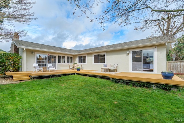 rear view of property with a yard, a chimney, stucco siding, fence, and a wooden deck