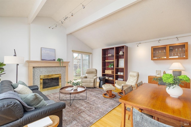 living area featuring vaulted ceiling with beams, a tiled fireplace, track lighting, and wood finished floors