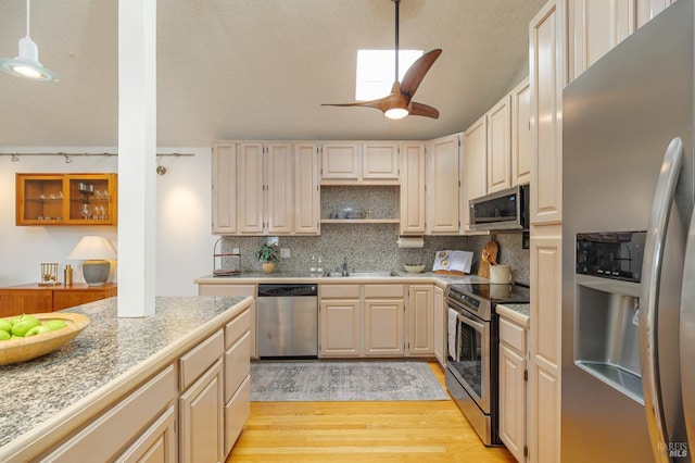 kitchen with a textured ceiling, a sink, appliances with stainless steel finishes, decorative backsplash, and light wood finished floors