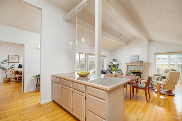 kitchen featuring tile countertops, light wood finished floors, a glass covered fireplace, and vaulted ceiling with beams