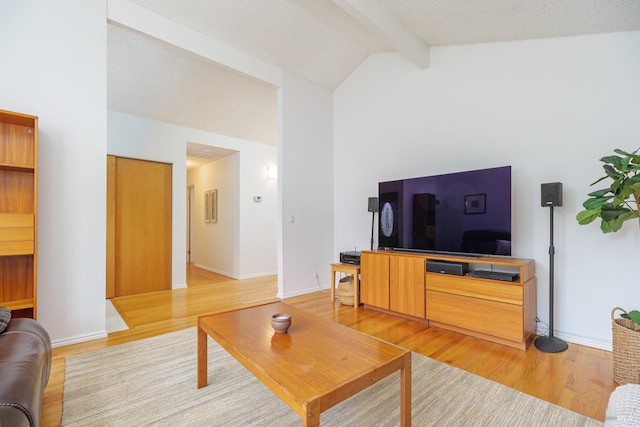 living room featuring vaulted ceiling with beams, a textured ceiling, baseboards, and light wood-style floors