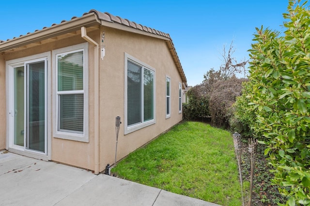 view of home's exterior with a patio area, a tile roof, a lawn, and stucco siding