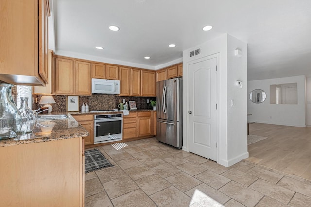 kitchen featuring visible vents, backsplash, stone counters, stainless steel appliances, and a sink