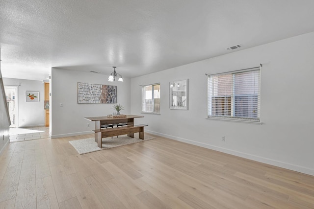 dining room featuring visible vents, a notable chandelier, a textured ceiling, light wood-style floors, and baseboards