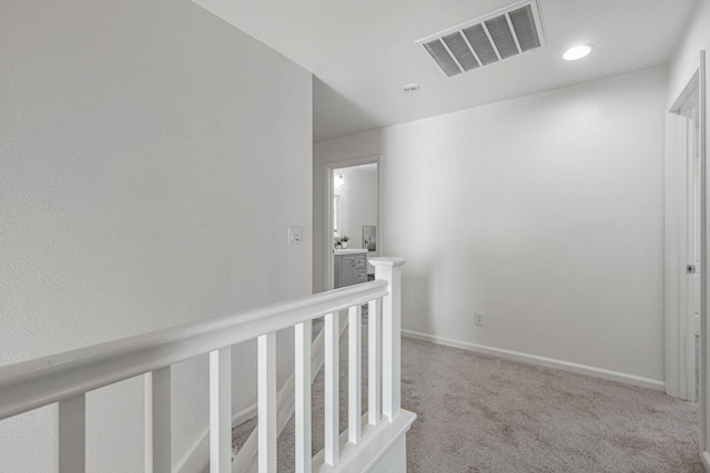 hallway with visible vents, an upstairs landing, carpet, and baseboards