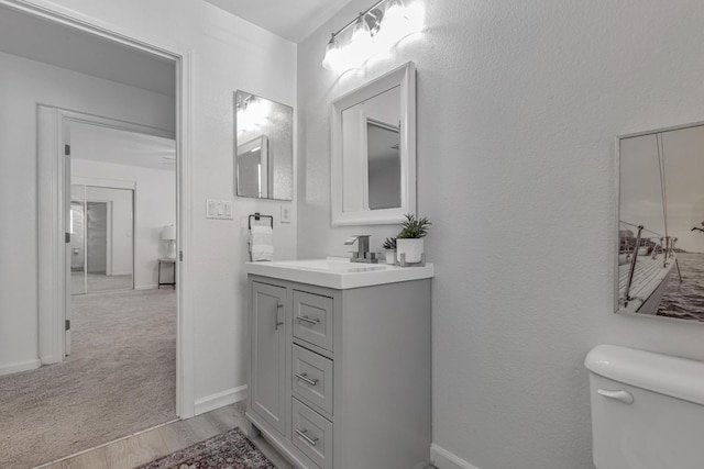 bathroom featuring baseboards, toilet, wood finished floors, and vanity