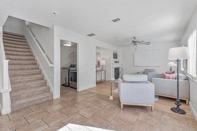 living area featuring stairway, a fireplace, visible vents, and ceiling fan