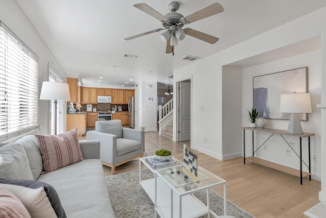 living area with visible vents, baseboards, light wood-style flooring, and stairway