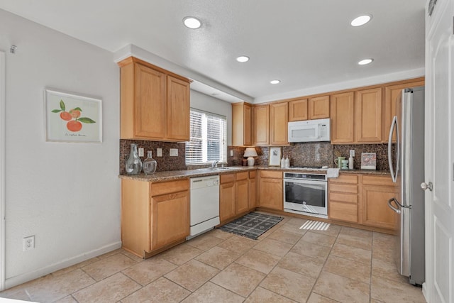 kitchen with a sink, backsplash, appliances with stainless steel finishes, stone counters, and baseboards